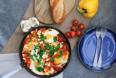 an omelet in a pan with tomatoes, garlic and bread on the side