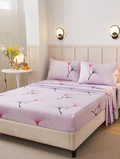 a bed with pink sheets and pillows in a white room next to a night stand