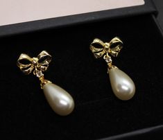 Golden bow studs with teardrop champagne pearl,cubic zirconia stone set,gold plated brass base metal. Pearls are made and manufactured on the island of Mallorca. SIZE GUIDE: pearl size wide - 8-9mm cubic zirconia size - 2mm pearl color - champagne MAINTENANCE - To keep your jewellery in good condition, we recommend that you do not come into contact with any chemicals, strong perfumes or water. All our products comes in a signature box and ready to gift. To see other size and color options click Golden Bow, Studs Gold, Pearl Color, Pearl Size, Gold Plated Earrings, Stone Settings, Base Metal, Jewelry Earrings Studs, Cubic Zirconia