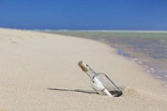 an empty glass bottle sitting on top of a sandy beach