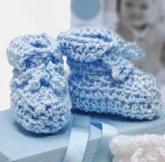 blue crocheted baby booties sitting on top of a box next to a teddy bear