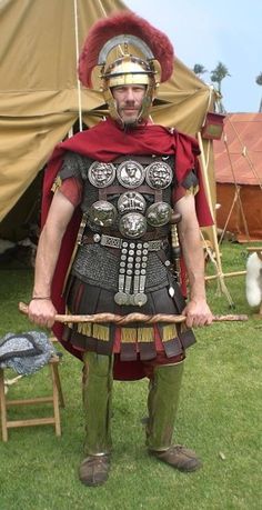 a man dressed in roman armor holding a bow and arrow while standing next to a tent