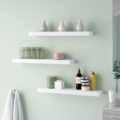 three white floating shelves in a bathroom with green walls and towels hanging on the wall