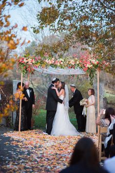 a bride and groom kissing under an arch with petals on the ground in front of them