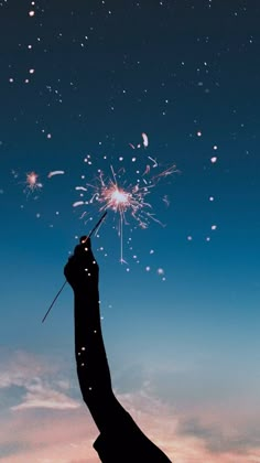 a hand holding a sparkler in the air at night with sky and clouds behind it