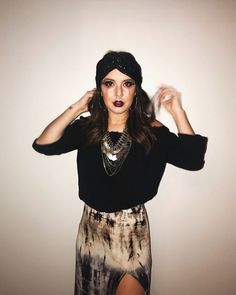 a woman posing with her hands on her head and wearing a black shirt, tie dye skirt and silver necklace