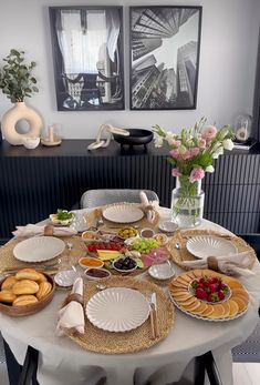 the table is set with plates and bowls of food on it, along with flowers in vases