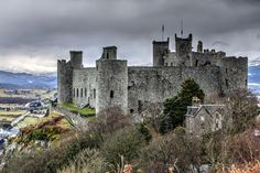 an old castle on top of a hill with snow capped mountains in the background and dark clouds overhead