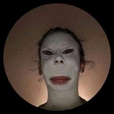 a woman with white makeup and dark make up looks at the camera in a circle