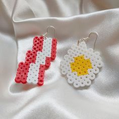 two pieces of white and red beaded earrings with yellow star on them sitting on a white cloth