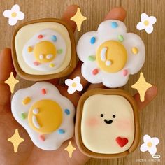 four decorated cookies in the shape of toast with smiley faces and stars on them are held by someone's hand