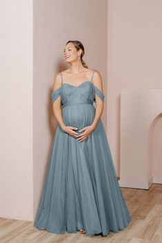 a pregnant woman in a blue dress standing against a wall