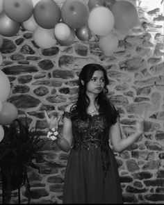 a woman standing in front of a stone wall with balloons hanging from it's ceiling