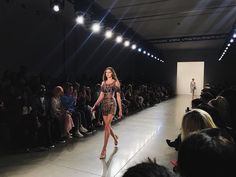 a model walks down the runway in front of a large group of people at an event