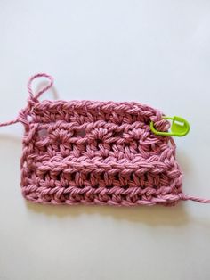 a pink crocheted object with a green hook on it's end and a white background