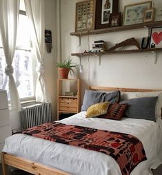 a bed sitting next to a window in a bedroom with white walls and wooden furniture