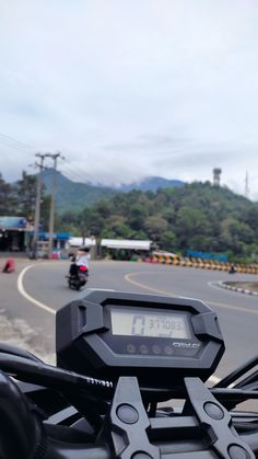 there is a digital clock on the handlebars of a motorcycle that is driving down the road