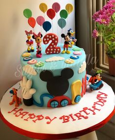 a birthday cake decorated with mickey mouse figures and balloons for a child's first birthday