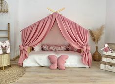 a pink canopy bed sitting on top of a wooden floor next to two dressers