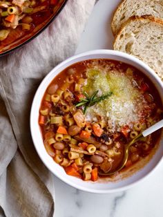 a bowl of pasta soup with bread on the side