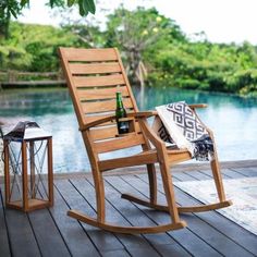 a wooden rocking chair sitting on top of a wooden deck next to a lake with a bottle of wine in it