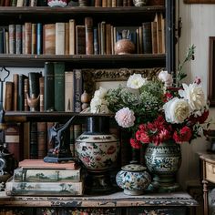 flowers in vases on top of an old dresser next to books and other antique items