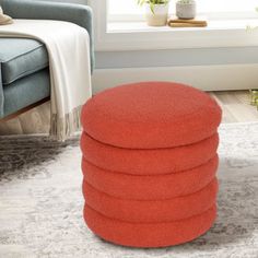 an orange ottoman sitting on top of a rug in front of a chair and window