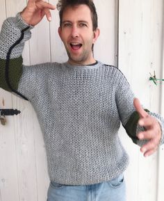 a man wearing a gray and green sweater pointing to the side with his hand on his hip