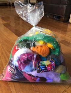 a plastic bag filled with lots of different colored yarn on top of a wooden floor