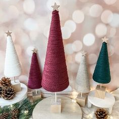 three small christmas trees sitting on top of a white table next to some pine cones