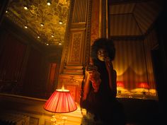 a woman standing next to a red lamp in a room with ornate walls and ceilings