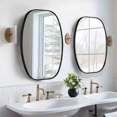 two oval mirrors mounted to the side of a white wall above double sinks in a bathroom