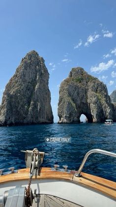 two large rocks in the middle of the ocean next to a boat on the water