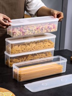 three plastic containers filled with pasta noodles on top of a black table next to a cutting board