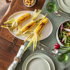 corn on the cob and other food items are laid out on a dining table