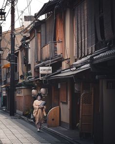 a woman walking down a street next to tall buildings