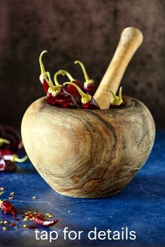 a wooden mortar bowl filled with small red peppers and a wooden spoon sitting on top of it