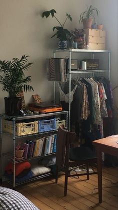 a room with a metal shelf filled with books and plants next to a bed covered in blankets