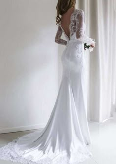 a woman in a white wedding dress looking down at her back and holding a bouquet