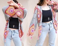 the woman is wearing a crocheted jacket and jeans with her hands on her hips