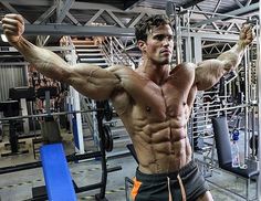 a shirtless man standing in front of a gym machine with his arms stretched out