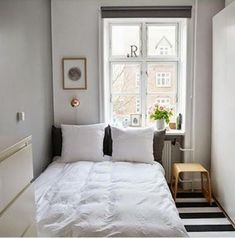 a small bedroom with a bed, dresser and window in the corner that has a black and white striped rug on it