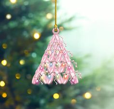 a pink christmas tree ornament hanging from a gold chain with lights in the background