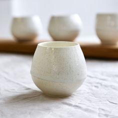 three white cups sitting on top of a table next to each other in front of a wooden tray