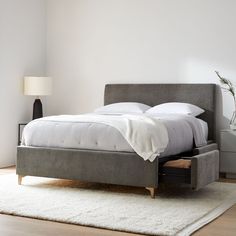 a bed with a storage drawer underneath it on a rug next to a nightstand and lamp