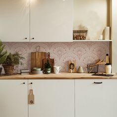 a kitchen with white cupboards and pink wallpaper on the back splash, along with wooden cutting boards