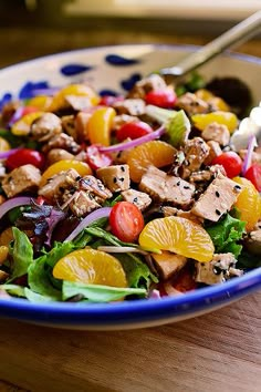 a salad with chicken, oranges, onions and lettuce in a blue bowl