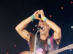 a man singing into a microphone while holding his guitar to his head with both hands