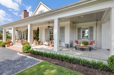 the front porch of a white house with lots of furniture on it's patio