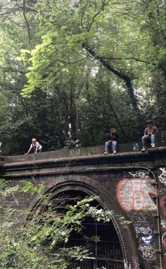 some people are sitting on the edge of a bridge in the woods with graffiti all over it